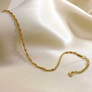 Detail of a gold stainless steel double layer anklet with a small heart charm on silk