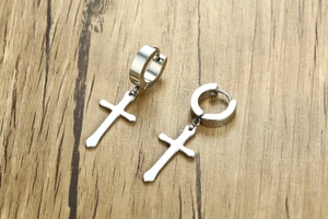 Macro view of polished silver stainless steel cross pendant earrings on wood texture