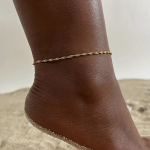 Detailed view of a gold-plated twisted rope anklet on a beach setting showing fine texture