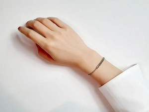 Detail shot of dainty silver beaded and link chain bracelet worn on wrist over white cuff