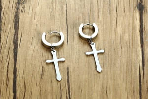 Macro shot of polished stainless steel hoop earrings with hanging cross charm on wood
