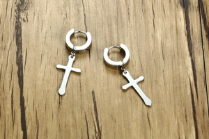 Close-up of silver stainless steel cross earrings on a natural wood surface