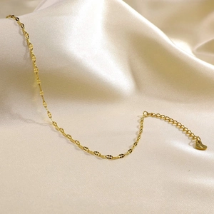 Detail of gold-plated stainless steel anklet with heart pendant on satin background