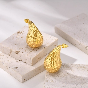 Macro detail of golden hammered waterdrop earrings on stone props for luxury display