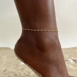 Detailed shot of a delicate gold wave chain anklet on a sun-kissed ankle for summer vibes