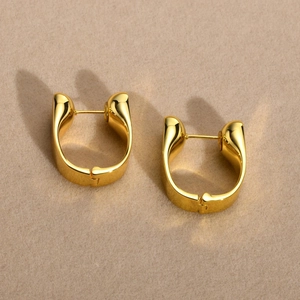 Polished gold U-shaped chunky geometric earrings on soft beige textured background