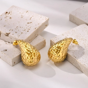 Detailed shot of golden water drop stud earrings with unique hammered metal texture