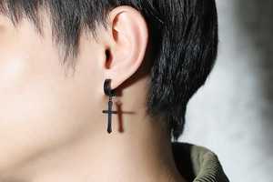 Close-up of black matte stainless steel cross earring worn by a model in soft side lighting