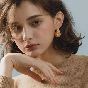 Golden hammer textured teardrop stud earrings in stainless steel on female model