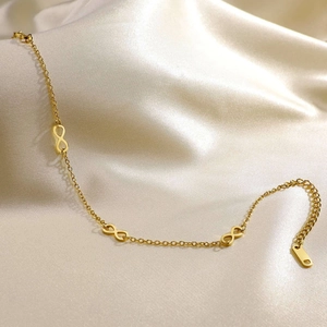 Detail of golden double-layer infinity anklet on elegant champagne silk background