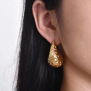 Macro shot of gold hammered teardrop earring showing textured metallic finish on ear