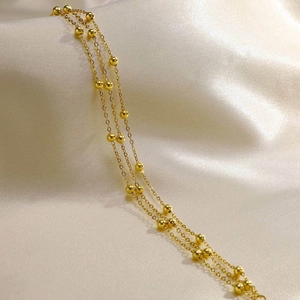 Macro shot of double-layered gold beaded anklet on elegant white satin fabric