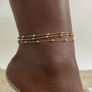 Detail of a triple-layer gold beaded anklet on an ankle over a minimal gray background