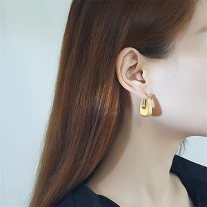 Gros plan de boucles d'oreilles dorées en U évidées avec une finition polie sur l'oreille