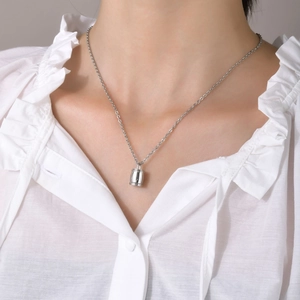 Gros plan d'un collier pendentif urne cylindrique argenté porté par un mannequin