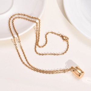 Détail macro du collier pendentif urne cylindrique doré avec chaîne fine et fermoir homard