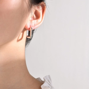 Close-up of polished silver geometric rectangular hoop earring worn by a model