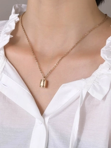 Collier pendentif urne cylindrique dorée minimaliste porté sur le cou avec un haut blanc