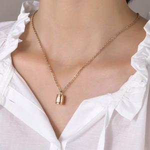 Gros plan d'un collier pendentif cylindre doré porté sur un chemisier blanc à volants