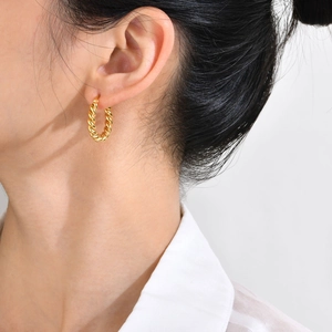 Close-up of golden twisted hoop earrings showing refined spiral texture and metallic shine