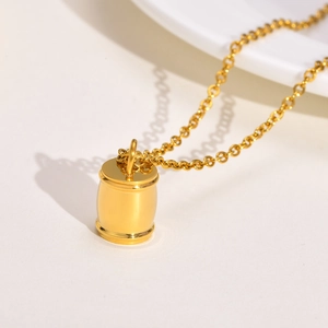 Vue macro d'un collier pendentif cylindrique doré sur un plateau en porcelaine blanche