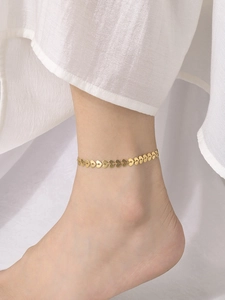Close-up of golden heart-shaped charm anklet on model's ankle with white fabric background
