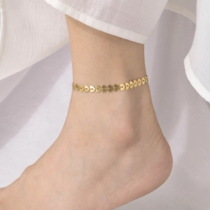Close-up of golden heart-shaped stainless steel anklet worn on woman's ankle