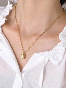 Gros plan d'un collier urne funéraire dorée porté par un mannequin en chemisier blanc