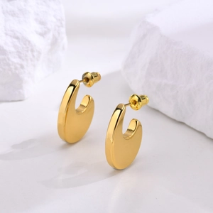 Macro shot of thick gold-plated U-shaped stud earrings on minimalist white stone display