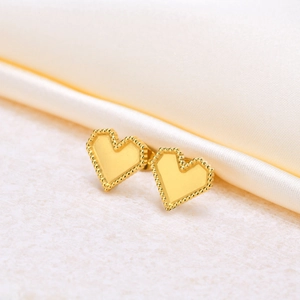 Minimalist gold heart earrings with beaded edge on a luxury silk and stone background