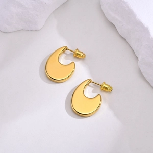 Detailed close-up of gold-plated U-shaped earrings on a white textured stone surface