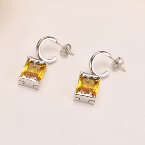Silver geometric earrings with square yellow zircon stones on a white textured background