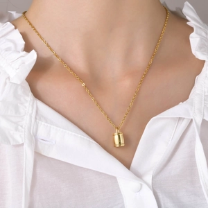 Détail d'un collier pendentif cylindrique doré minimaliste porté par un mannequin en blanc