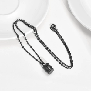 Gros plan du pendentif urne cylindrique en acier noir avec sa chaîne sur fond blanc
