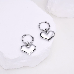 Gros plan des boucles d'oreilles cœur en argent poli sur une pierre blanche texturée