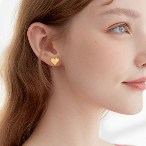 Minimalist gold heart stud earrings with milgrain edges on female model ear