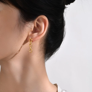 Boucles d'oreilles dorées en acier titane à trois anneaux ovales portées par un mannequin