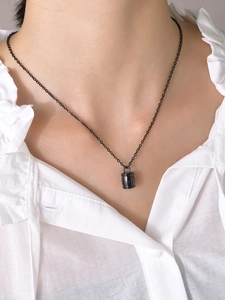 Pendentif urne cylindrique noir poli sur collier, porté sur un chemisier blanc