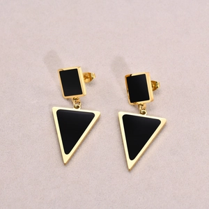 Close-up of golden geometric earrings with black triangular pendants on beige fabric