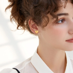 Close-up of golden heart stud earrings with beaded edge on a model's ear