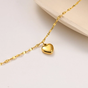 Macro detail of polished gold heart pendant with shimmering sequin-style chain link