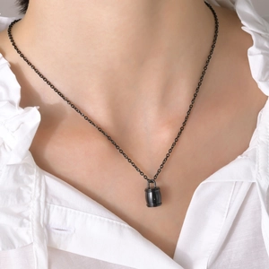 Gros plan d'un collier à pendentif urne noire polie porté sur une chemise blanche