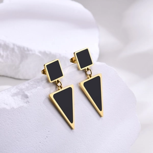 Detail view of geometric gold triangle earrings with matte black inlay on textured background