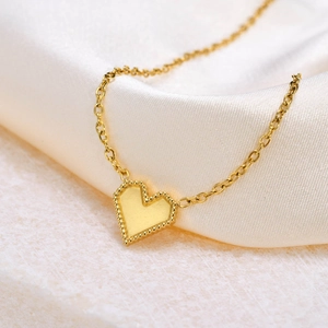 Close-up of golden heart pendant with beaded edge on white textured stone and silk