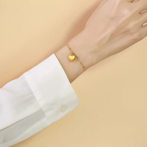 Close-up of a delicate golden heart pendant bracelet worn over a white shirt sleeve