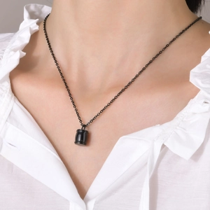 Gros plan du collier urne cylindrique en acier inoxydable noir sur chemise blanche