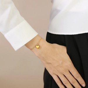 Detailed shot of a gold heart pendant bracelet worn by a model in a minimalist style