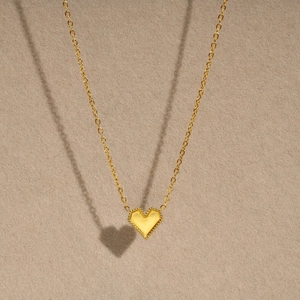 Detail view of a gold heart pendant with beaded edges on a minimalist necklace chain
