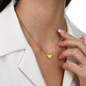 Close-up of a gold heart necklace with beaded edges worn on a neck with a white blazer