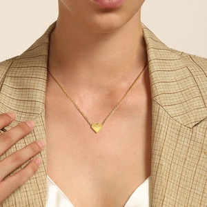 Detailed view of a gold heart pendant necklace with beaded edges on a model in a beige suit